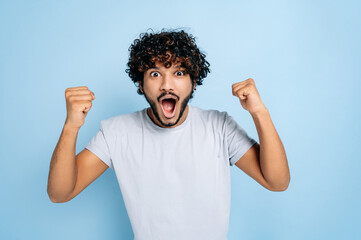 Enthusiastic amazed indian or arabic guy, in abasic t-shirt, rejoices in success, victory, win,...