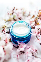 Obraz na płótnie Canvas Herbal spa cosmetic cream with pink cherry flowers in a blue glass jar. Hygienic skincare lotion product.