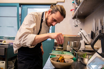 Fototapeta na wymiar chef cocina plato de tempura de verduras con tinta de calamar y salsa de pimiento rojo en cocina de restaurante en un bol 