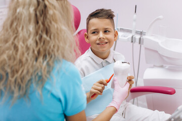 Female dentist shows a boy on a mock-up how to brush his teeth properly