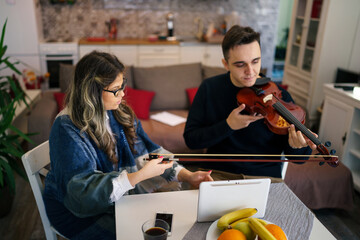 Young adult caucasian man student learning to play violin with help of his professor woman female mentor teaching him how to improve skill at home explaining lesson real people private class concept