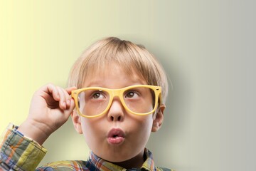 Funny little child boy in glasses looking in camera on yellow background.  Education for smart...