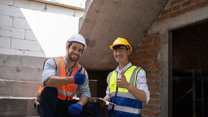 Two young engineers of different nationalities, Asian, Middle Eastern, Turkish, are working on a project together at a house and building construction site.
The worker is giving thumbs up and smiling.