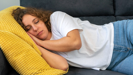 Sleeping woman with curly hair taking nap on sofa during the day at apartment