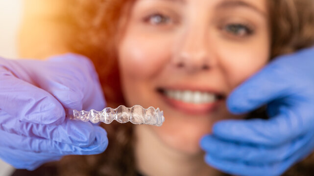 Dentist in gloves applying invisible aligner on female patient teeth at clinic