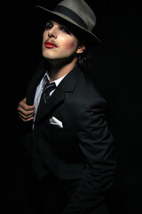 Portrait of young elegant gay male with hat, suit, tie, make up on face and lipstick posing with fashion style for camera. Vertical. Copy space.