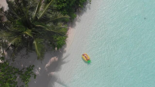 Aerial drone quad copter footage of nice woman girl floating on a lilo inflatable with in tropical waters in maldives of crystal clear waters of an ocean coral reef with palms