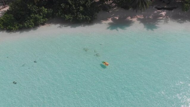 Aerial drone quad copter footage of nice woman girl floating on a lilo inflatable with in tropical waters in maldives of crystal clear waters of an ocean coral reef with palms