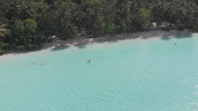 Aerial drone quad copter footage of nice woman girl floating on a lilo inflatable with in tropical waters in maldives of crystal clear waters of an ocean coral reef with palms