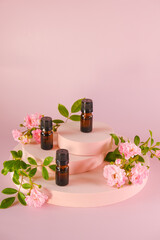 Rose essential oil.Aromatherapy and cosmetics. brown bottles set and pink rose flowers on a pink podium on light pink background.Organic natural rose oil.Organic bio cosmetics.Rose oil 