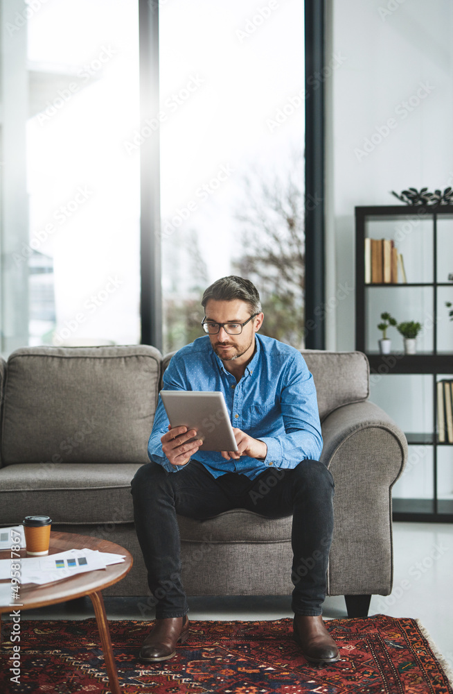 Poster the tool of his trade. shot of a businessman using his digital tablet while sitting on a sofa in the