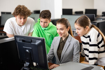 Modern interested teen schoolchildren learning basics of programming with friendly female teacher in computer college..