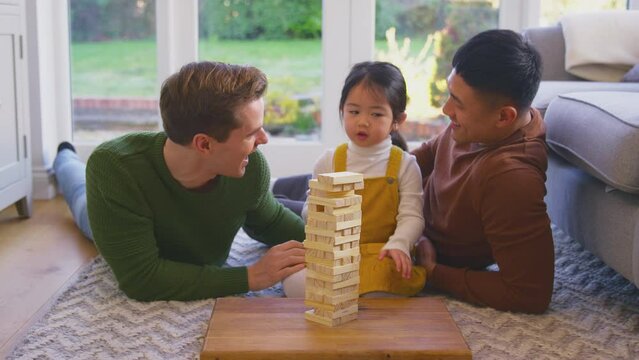 Family with two dads playing game with daughter at home stacking wooden bricks into tower - shot in slow motion