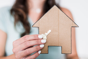 Fototapeta na wymiar first time home buyers, woman holding cardboard house icon and key towards the camera