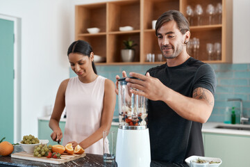 This is gonna taste amazing. Cropped shot of an affectionate young couple making smoothies in their...