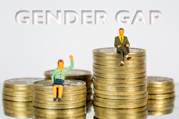 Miniature people sitting on a pile of coins. The concept of income distribution gender gap. Macro