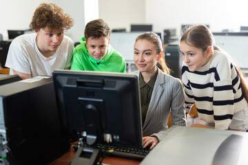 Interested teenagers studying with young female teacher in information technology class at college, sitting around one computer