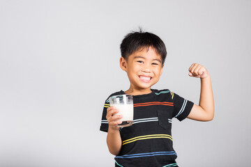 Little cute kid boy 5-6 years old smile holding milk glass and show power strong gesture in studio...