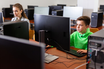 Modern preteen boy learning basics of programming in group course in computer college..