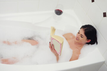 Relaxing in the tub. Cropped shot of a young woman relaxing in the bathtub with a book and glass of wine.