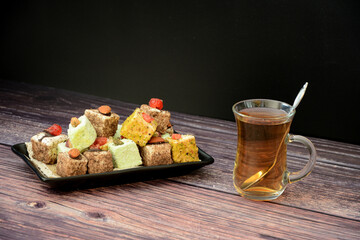 A variety of Turkish sweets on a plate and a cup of hot tea on a wooden table.