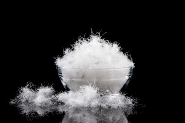 soft fluffy down feather in glass bowl on black background.