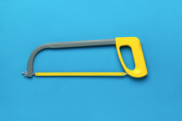 Hand hacksaw on metal with a yellow handle on a blue background. Flat lay.