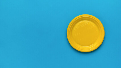 Plastic yellow plate on a blue background. A place for your text. Flat lay.