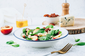 Healthy summer salad with spinach, peach, pecan nuts, blue cheese on white background