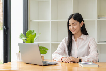 Portrait of a happy Asian woman smiling happily relaxing sitting on a chair. Independent young Asian hipster girl using laptop computer in coffee shop work-study concept