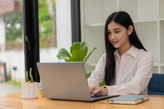Portrait of a happy Asian woman smiling happily relaxing sitting on a chair. Independent young Asian hipster girl using laptop computer in coffee shop work-study concept