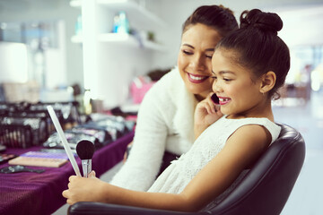 Look how pretty you are. Shot of a mother helping her cute little girl to apply makeup in a dressing room.