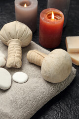 Bathing towel with spa stones, herbal bags and aroma candles on dark background