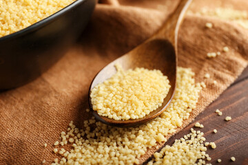 Spoon with raw couscous on table