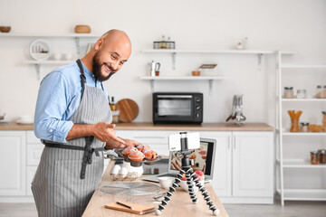 Handsome man with tasty peach muffins recording video in kitchen