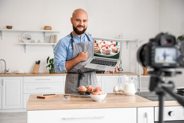 Fototapeta na wymiar Handsome man with laptop and peach muffins in kitchen