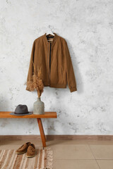 Wooden bench with hat, vase, shoes and jacket hanging on light wall