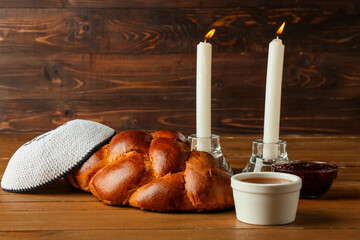 Traditional challah bread with glowing candles and Jewish cap on wooden background. Shabbat Shalom - obrazy, fototapety, plakaty
