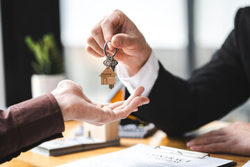 Real estate agent business man holding house key to his client after signing contract agreement in...
