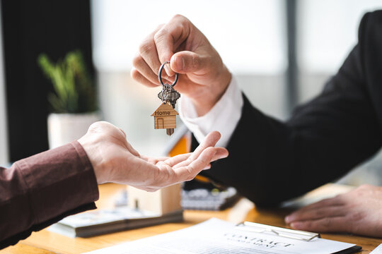 Real estate agent business man holding house key to his client after signing contract agreement in office,concept for real estate, moving home or renting property