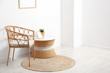 Stylish interior of room with wicker chair and table near light wall