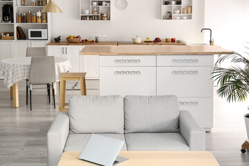 Interior of light modern kitchen with white counters, dining table and sofa