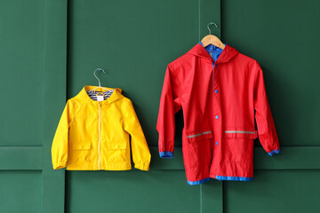 Child's raincoats hanging on green wall