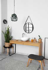 Wooden table with sink and bath supplies near light wall in room