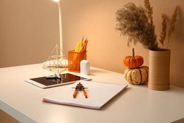 Notebook, compass, tablet computer and earphones on table near color wall