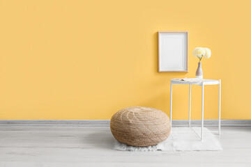 Table with flowers in vase and pouf near yellow wall