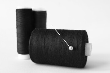 Black sewing thread spools with pin on white background