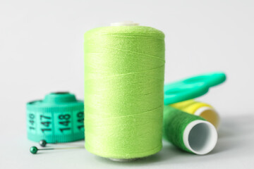 Sewing thread spools, measuring tape and scissors on light background