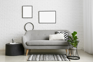 Interior of room with sofa, houseplant and blank photo frames on white brick wall