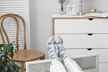 Woman in soft socks warming feet near radiator. Concept of heating season
